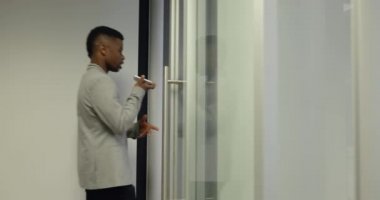 Koridorda akıllı bir telefonla yürüyen Afro-Amerikalı bir adamın yan görüntüsü ve modern bir ofiste oturup konuşan Kafkasyalı bir kadın ve melez bir ırk adamının görüntüsü.