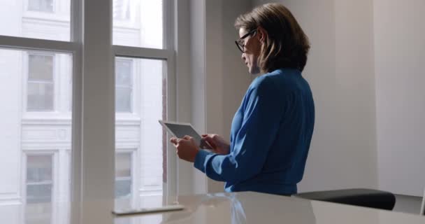 Vue de côté gros plan d'une professionnelle caucasienne debout près de la fenêtre dans un bureau moderne à l'aide d'une tablette 