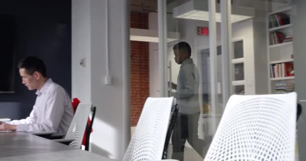 廊下を歩いているアフリカ系アメリカ人の男性の側面図と現代のオフィスでの会議で混合人種の男と話をノートパソコンを使用して白人女性に参加し 建築図面が壁に表示されます — ストック動画