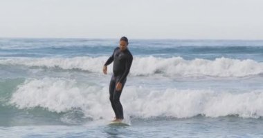 Kafkasyalı bir adamın sığ sularda sörf yaparken ön görüntüsü. Yavaş çekimde çekilmiş.