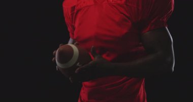 Afrika kökenli Amerikalı erkek bir Amerikan futbolcusunun ön görüntüsü. Takım üniforması giyiyor ve elinde futbol topu tutuyor. Ağır çekimde.