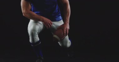 Kafkas asıllı Amerikalı bir futbolcunun yakın çekimde omuz vatkaları ve kasklarıyla takım üniforması giyip tek bacağının üzerine çöküp kafasına futbol topu dayadığı ve başını kameraya doğru eğdiği görülüyor.