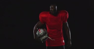 Afrika kökenli Amerikalı erkek bir Amerikan futbolcunun takım üniforması, pedleri ve göz siyahı giymiş, kaskı kolunun altında duruyor.