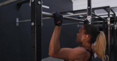 Spor kıyafetleri giymiş sporcu bir kadının spor salonunda barfiks çekerken yan görüntüsü.