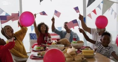 Bağımsızlık Günü yemeği için bayraklarla süslenmiş, bayraklarla sallanan ve balonlarla oynayan Afrika kökenli, çok nesilli bir ailenin yemek masasının etrafında oturduğu ön manzara.