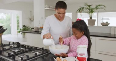 Gülümseyen Afro-Amerikan bir kadın ve küçük kızının mutfakta krep yaparken, malzemeleri karıştırma kabına koyarken, anne sütü dökerken ve kız karıştırırken, yavaş çekimde