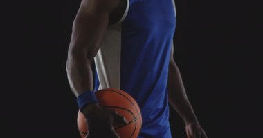Takım renkleri giymiş, kaslı, Afro-Amerikan bir basketbolcunun portresi. Bir elinde basketbol topu tutuyordu ve kameraya bakıyordu, yavaş çekimde.