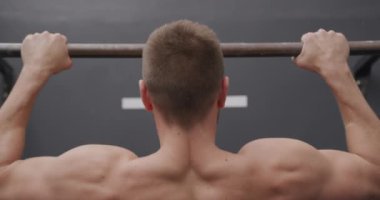 Spor salonunda antrenman yapan üstsüz, beyaz bir adamın barın üstünde barfiks çekişini yakından çek.