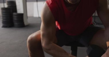 Spor kıyafetleri giyen, spor salonunda çapraz antrenman yapan, halterle kıvırcık saçlı, ağır çekimde spor yapan beyaz bir adamın ön görüntüsü.