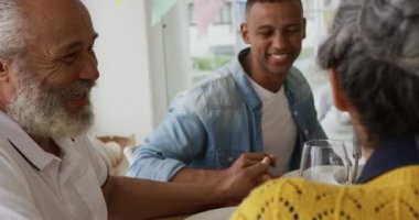 Afrika kökenli yaşlı bir adamın karısı ve yetişkin oğluyla konuşurken yemek masasında otururken gülümsemesinin yan görüntüsü.
