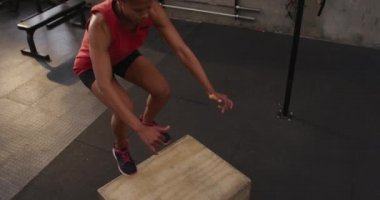 Spor kıyafetleri giymiş, spor kıyafetlerini giymiş, spor salonunda hoplayıp zıplayan, ağır çekim bir kadının yüksek açılı görüntüsü.