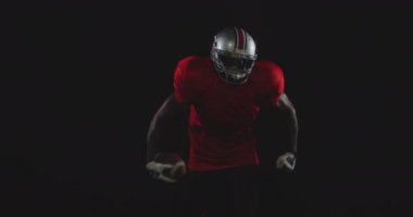 Afrika kökenli Amerikalı erkek bir Amerikan futbolcunun takım üniforması, pedleri ve kaskı vardı elinde bir futbol topuyla, ağır çekimde ilerliyordu.