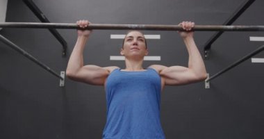 Spor kıyafetleri giymiş, spor kıyafetleri giymiş spor salonunda barın üstünde barfiks çeken, ağır çekimde barfiks çeken beyaz bir kadının ön görüntüsü.