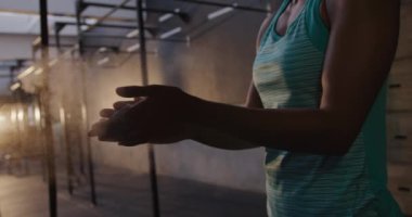 Spor kıyafetlerini giymiş, spor salonunda çapraz antrenman yapan, ağırlık kaldırmaya hazırlanmak için ellerine tebeşir süren bir kadının orta kesimi.