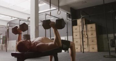 Spor salonunda antreman yapan, halterleri kaldıran, ağır çekimde ağırlık kaldıran üstsüz beyaz bir adamın alçak açılı yan görüntüsü.