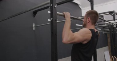 Spor kıyafetleri giyen, spor salonunda çapraz antrenman yapan barlarda barfiks çeken beyaz bir adamın yan görüntüsü.