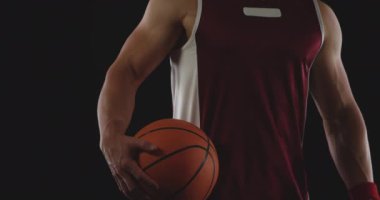 Kaslı beyaz erkek basketbolcunun portresi. Takım renginde. Bir elinde basketbol topu var ve kameraya bakıyor.