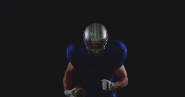 Kafkas asıllı Amerikan futbolcusunun takım üniforması, pedleri ve kaskı var, elinde futbol topu var ve yavaş çekimde koşuyor.