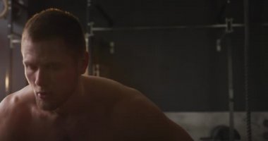 Spor salonunda antrenman yapan, derin nefes alan, esneyen, yavaş çekim yapan üstsüz, beyaz bir adamın ön görüntüsü.