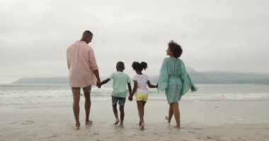 Sahile doğru yürüyen Afrikalı bir çiftin, genç oğulları ve kızlarıyla el ele tutuşmalarını, yavaş çekimde.
