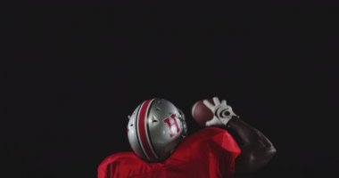 Afrika kökenli Amerikalı erkek bir Amerikan futbolcunun takım üniforması, pedleri ve kaskı var. Bir elinde futbol topu tutuyor ve kolunu zaferle kaldırıyor.