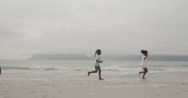 Gülümseyen Afrikalı Amerikalı bir çiftin deniz kenarında bisiklet sürüşünün yan görüntüsü. Genç kızları ve oğulları önlerinde koşuyor, ağır çekimde.