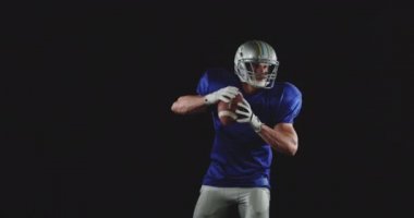 Kafkas asıllı Amerikan futbolcusunun takım üniforması, pedleri ve kaskı var elinde futbol topu, etrafa bakıyor ve blöf yapıyor, ağır çekim.