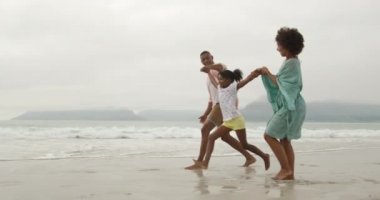 Gülümseyen Afro-Amerikan bir çiftin deniz kenarında yürürken aralarında genç kızlarıyla el ele tutuşurken ve onu yavaşça havaya kaldırırken görüntüsü.