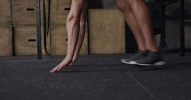 Spor salonunda çapraz antrenman yapan üstsüz, beyaz bir adamın yan görüntüsü. Burpee yapmak için aşağı iniyor, kalkıyor ve koşuyor, ağır çekim.