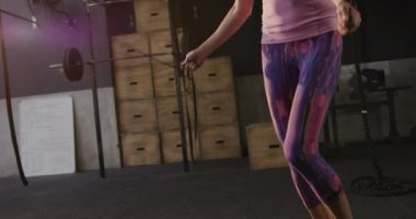 Spor kıyafetleri giymiş, spor kıyafeti giymiş, spor salonunda iple atlayan, ağır çekimde hoplayıp zıplayan beyaz bir kadının alçak açılı görüntüsü.