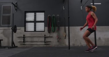 Spor kıyafetleri giymiş, spor kıyafetlerini giymiş spor salonunda koşan ve yere dokunan bir kadının yan görüntüsü.