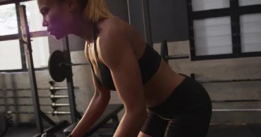 Spor kıyafetleri giyen, spor salonunda çapraz antrenman yapan, dambıllarla yükselen, yavaş çekim yapan bir kadının yan görüntüsü.