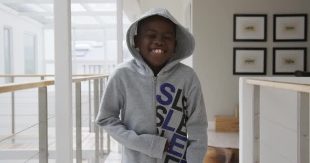 若いアフリカ系アメリカ人の少年の肖像画 自宅のシッティングルームでは パーカーを着て カメラを見て笑って スローモーション — ストック動画
