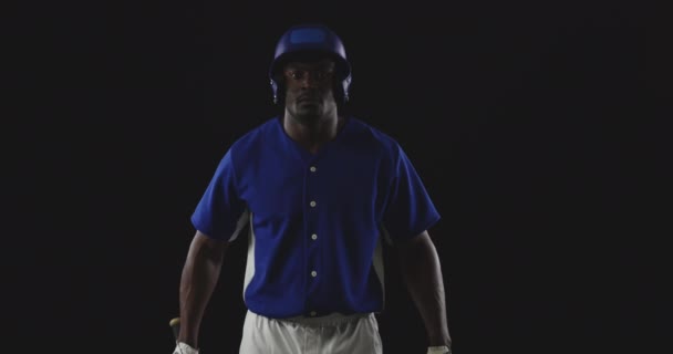 チームのユニフォームを着たアフリカ系アメリカ人男性野球選手の肖像とヘルメット カメラを探して 彼の肩の上に野球バットを休ませます スローモーション — ストック動画