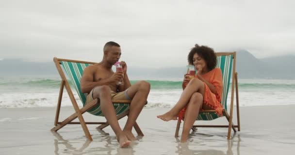 Вид Спереди Афроамериканскую Пару Пляже Моря Сидящую Шезлонгах Пьющую Коктейли — стоковое видео