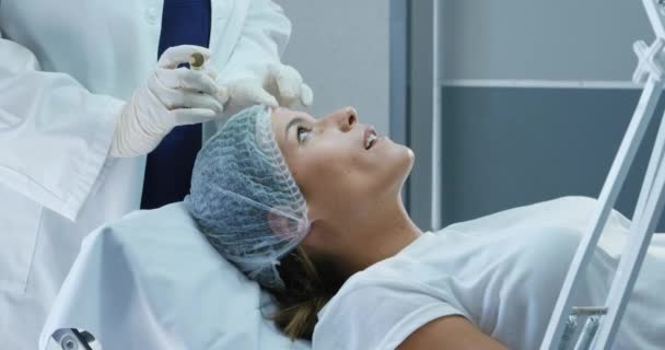 一名白种人妇女头戴一顶帽子躺下 医生在诊所给她的额头打针时的侧影 — 图库视频影像