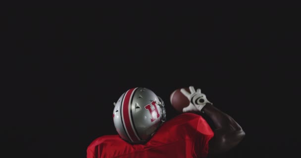 チームのユニフォーム パッド ヘルメットを着用し 片手でサッカーを保持し 勝利で彼の腕を上げるアフリカ系アメリカ人男性アメリカンフットボール選手の後部ビュー スローモーション — ストック動画