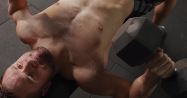 一个赤身裸体的白人运动员在一个健身房里交叉训练的高角镜头 他躺在长椅上提起哑铃 动作缓慢 — 图库视频影像