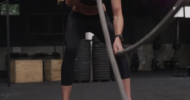戦闘ロープを使ったジムでスポーツウェアを身につけた白人女性のフロントビュー スローモーション — ストック動画