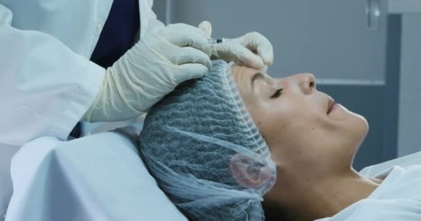 一名白人妇女头戴一顶帽子躺在床上 医生在诊所给她的额头注射肉毒杆菌毒素时的侧视图 — 图库视频影像