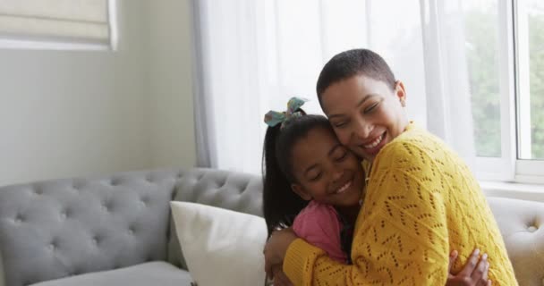 リビングの自宅にいるアフリカ系アメリカ人の女性と彼女の若い娘の笑顔の側面図は ソファの上に座っ抱擁と笑顔 スローモーション — ストック動画
