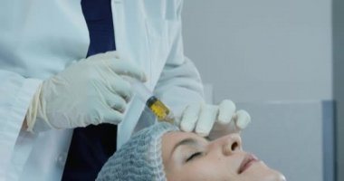 Sarık takan melez bir kadın klinikte alnına iğne yaparken beyaz bir kadının başlık takıp uzanması.