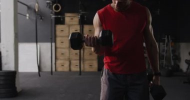 Spor kıyafetleri giyen beyaz bir adamın spor salonunda iki dambılla kıvırcık ve ağır çekimde yaptığı antrenmanın ön görüntüsü.