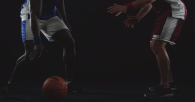 Kafkas erkek basketbolcunun, takım renkleri giymiş, rakip takımda oynayan Afrikalı Amerikalı bir erkek oyuncunun top sürüşünü engellemeye hazırlanan yan görüntüsü.