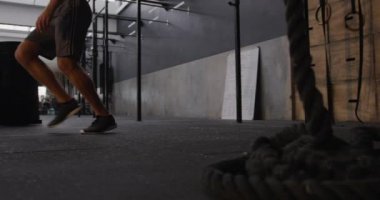 Spor kıyafetleri giyen beyaz bir adamın spor salonunda çapraz antrenman yaparken, bir yandan diğer yana koşarken ve yere dokunurken yan görüntüsü, ağır çekim.
