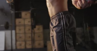 Spor salonunda çapraz antrenman yapan üstsüz, beyaz bir adamın orta kesimine bir ip ve ağır çekimde zıplıyor.
