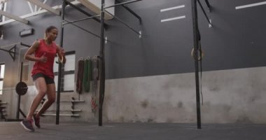 Spor kıyafetleri giymiş, spor kıyafetleri giymiş, spor salonunda koşan, zıplayan, ağır çekim bir kadının alçak açılı yan görüntüsü.