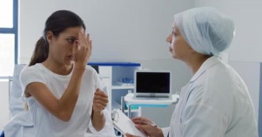 Bir hastanede muayene sırasında, beyaz bir kadın hastayla konuşan ve muayene eden melez bir kadın doktorun yan görüntüsü.