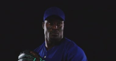 Önde, takım üniforması, beyzbol şapkası ve eldiven takan, beyzbol topu fırlatan, yavaş çekim yapan Afrikalı Amerikalı bir beysbol atıcısını görüyorsunuz.