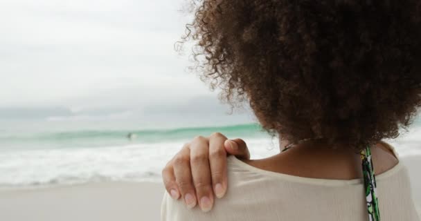 一个非裔美国妇女站在海滩上 手搭在肩上放松 转身面对镜头 慢吞吞地笑着 从肩膀上看过去 — 图库视频影像